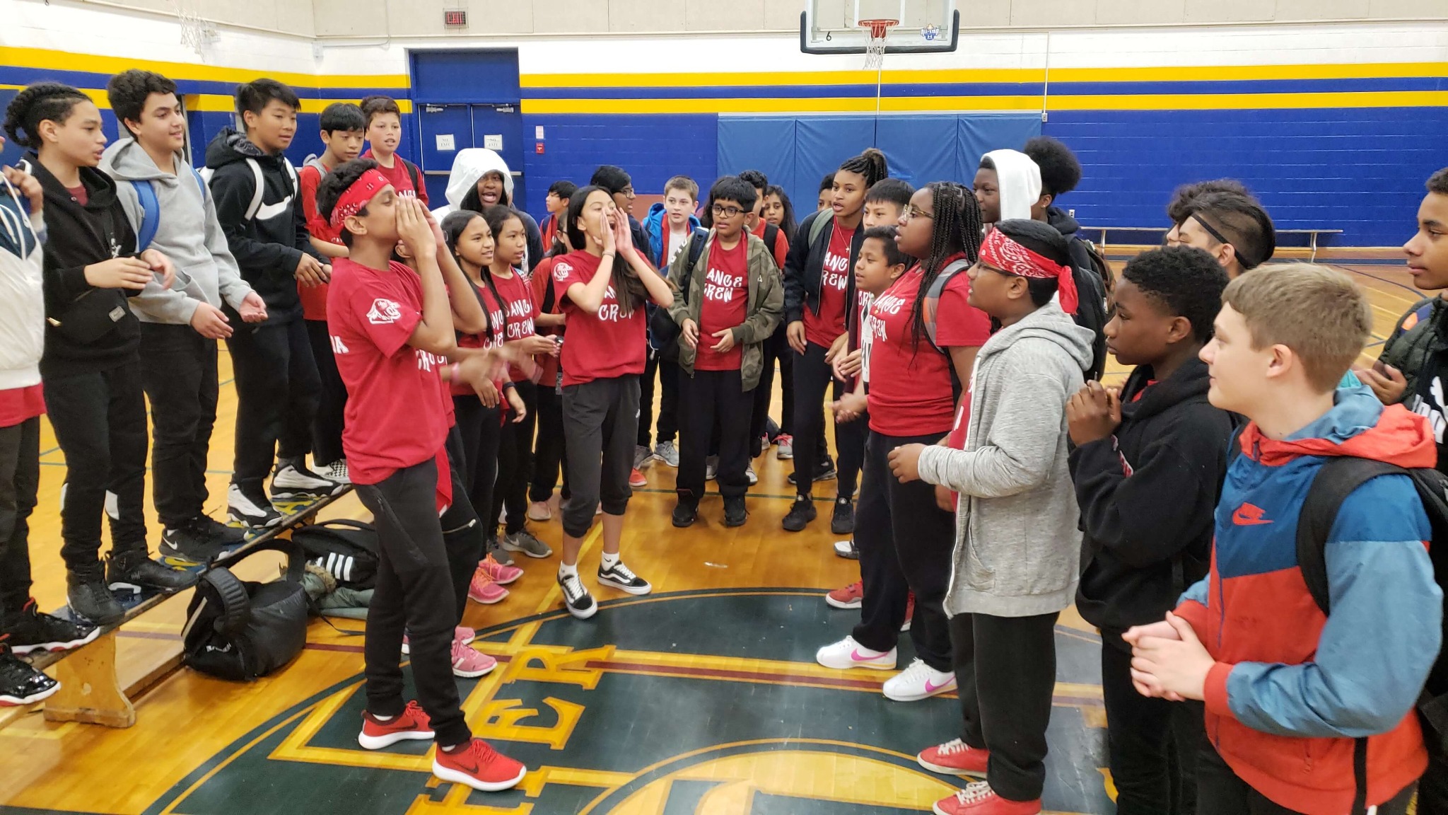 Students in red shirts leading a school cheer in a gym